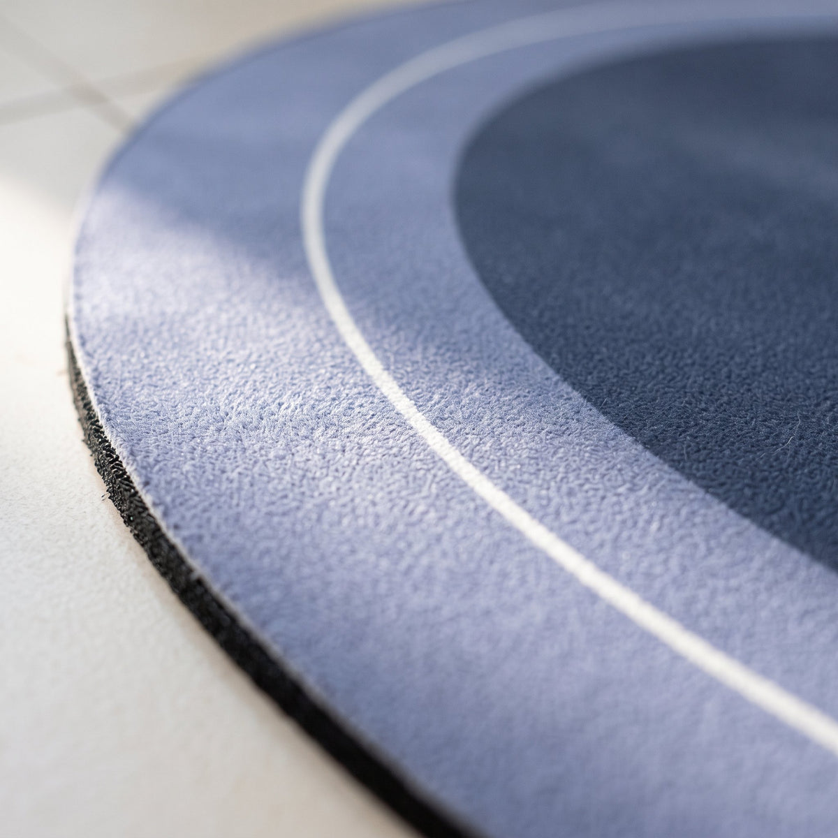 Detalle de la textura suave de la alfombra de baño, con sus dos tonos de azul y la línea blanca.