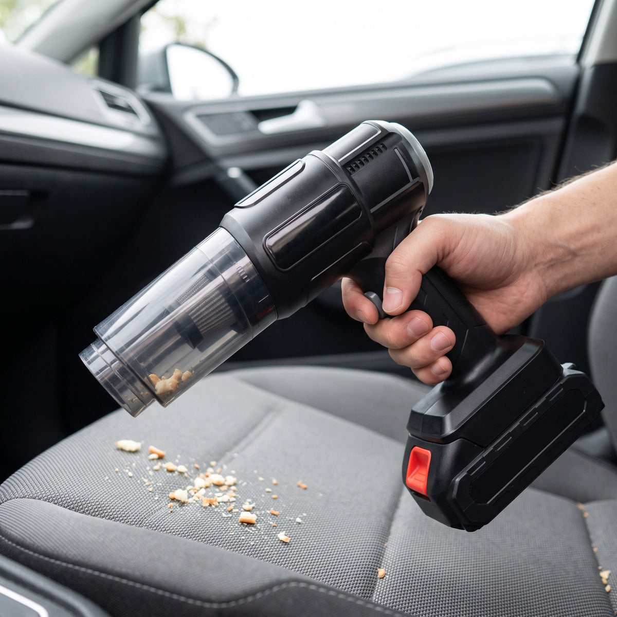 Mano aspirando migas del asiento de un auto con la aspiradora inalámbrica negra.