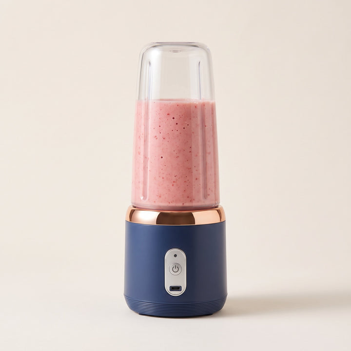 Licuadora portátil azul marino con vaso transparente lleno de batido rosado, vista de tres cuartos sobre fondo claro.