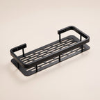 Repisa adhesiva para ducha de aluminio negro mate con base ranurada, sobre fondo blanco hueso.