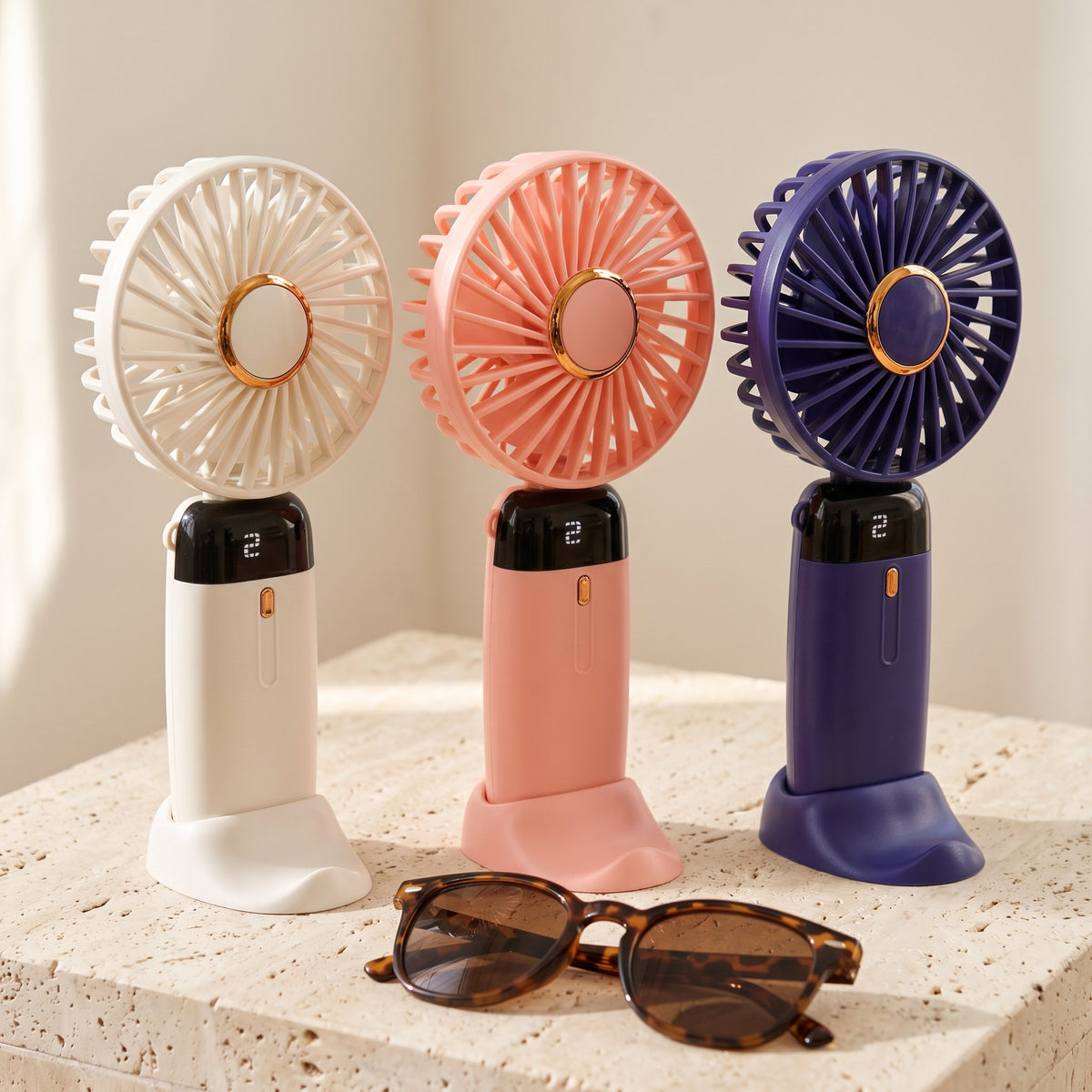 Los tres colores del ventilador portátil: blanco, rosado y púrpura (tono índigo), con lentes de sol para la escala.