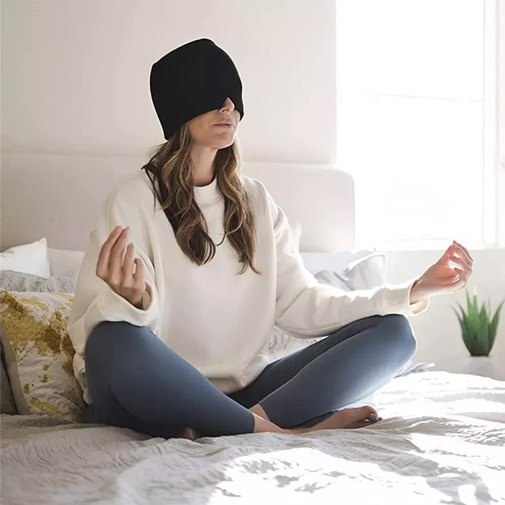 Mujer meditando en una cama con el gorro de gel para migraña cubriéndole los ojos.